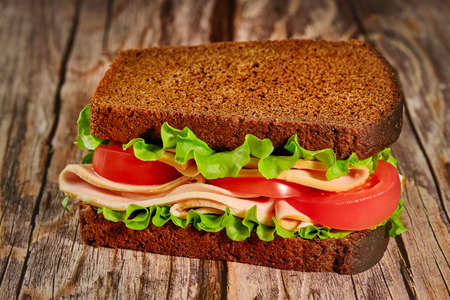 sandwich with black bread, tomatoes and sausage lies on a table made of rough boards, rustic style, organic foodの写真素材