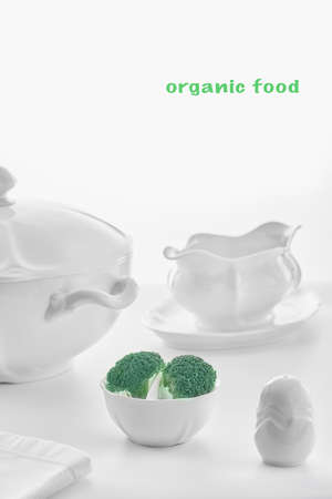 white porcelain dishware on a white background: soup tureen, gravy bowl, salt shaker and small plate with green broccoli, high key, shallow depth of fieldの写真素材