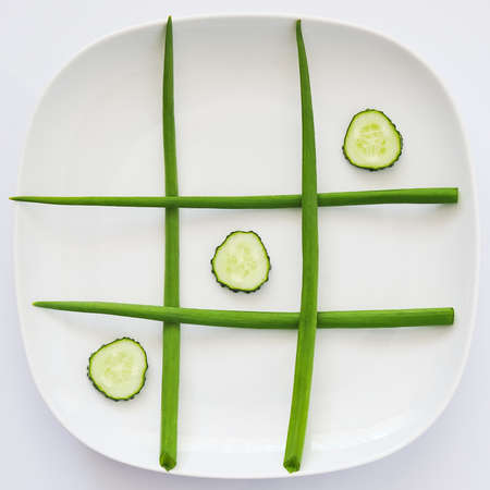 tic-tac-toe plate: green onions and cucumber wedges, white backgroundの写真素材