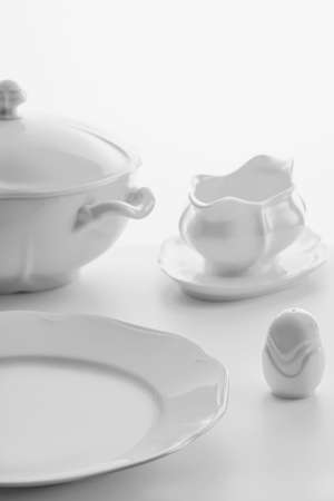 white porcelain dishware on a white background: soup tureen, gravy bowl, salt shaker and large plate, high key, shallow depth of fieldの写真素材