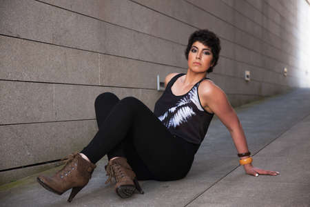 beautiful young woman, looking to camera, sitting on the floor, with a wall from background, outsideの写真素材