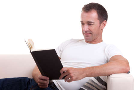 middle-age man lying on the sofa reading a book, isolated on white background, studio shot.の写真素材