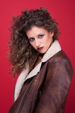 beautiful woman with curly hair, with fall and winter clothes, on red, studio shotの写真素材