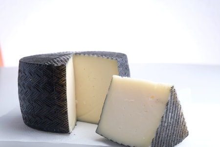 A piece of cheese lies next to the round head of cheese, cheese in black wax