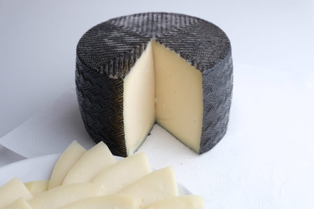 Chopped cheese lies on a plate next to the round head of cheese, cheese in black waxの写真素材