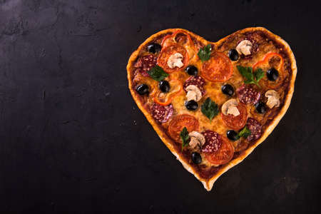 Pizza heart love Valentines Day romantic Italian restaurant dinner food. Prosciutto, olives, tomatoes, parsley, basil and mozzarella cheese meal on blackの写真素材