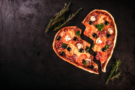 Heart shaped pizza with tomatoes and mozzarella for Valentines Day on vintage black background. Food concept of romantic heartbreak loveの写真素材