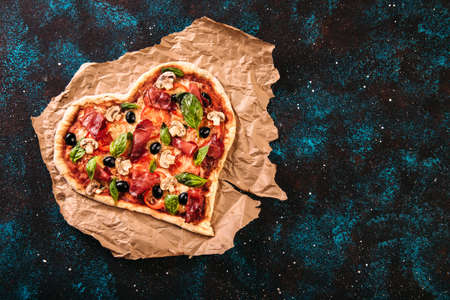 Heart shaped pizza with tomatoes and prosciutto for Valentines Day on vintage black turquoise background. Food concept of romantic loveの写真素材