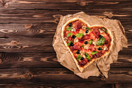 Heart shaped pizza with tomatoes and prosciutto for Valentines Day on vintage wooden background. Food concept of romantic loveの写真素材