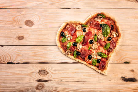 Heart shaped pizza with tomatoes and prosciutto for Valentines Day on vintage wooden background. Food concept of romantic loveの写真素材