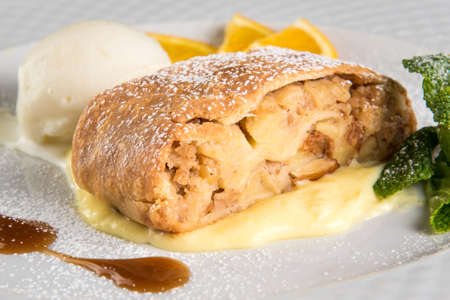 Apple strudel with ice cream and orange on white plateの写真素材
