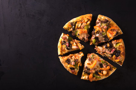 Cut into slices delicious fresh pizza with mushrooms and pepperoni on a dark background. Top view ....