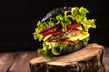 Delicious homemade vegan black burger with two chickpea cutlets, tomatoes, cheese, onion and salad on wooden table, dark background.の写真素材
