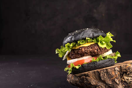 Black homemade delicious hamburger with dark bun, beef meat cheese lettuce onion, tomato on dark backgroundの写真素材
