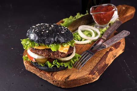 Fresh homemade burger on wooden serving board with fork and knife tomato sauce on dark backgroundの写真素材