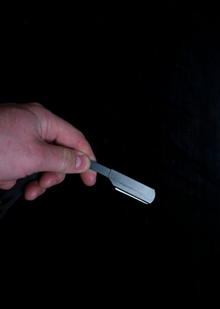 Man's hand holding a razor blade on a black background, close upの写真素材