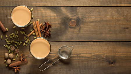 Two mugs with masala tea stand on a wooden table with spices. Top view. Copy space.の写真素材