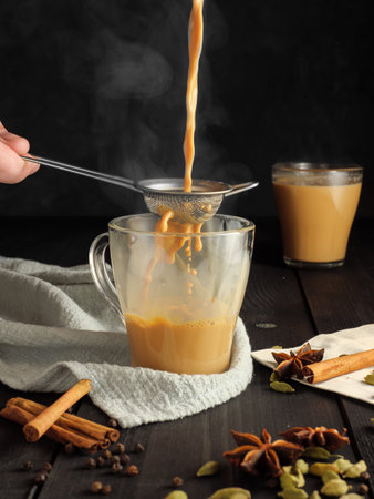 Masala tea is poured through a sieve into a glass mug. Species are on the table.の写真素材