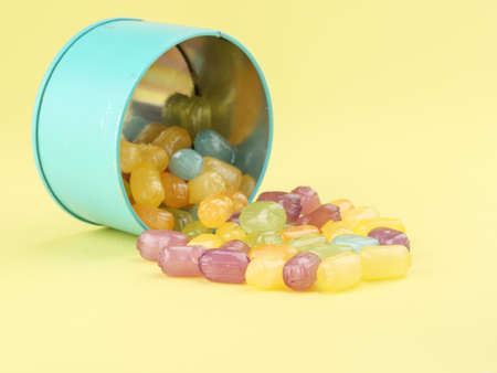 Multicolored caramel candies in a blue tin can on a yellow background.の写真素材