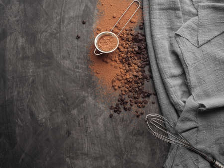 Chocolate chips, cocoa powder, a pastry whisk lies on a gray background with a gray cloth. Copy space. Top view.の写真素材