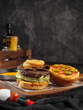 Burger with onion rings, cheese sauce and jalapeno peppers, hot sauce. Vertical photo, copy space.の写真素材