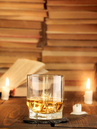 A glass of whiskey on the table with books and burning candles and rays of light. Copy space, vertical photo.の写真素材