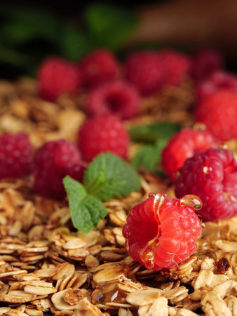 Raspberries lie on granola with mint leaves and honey drops. Vertical photo.