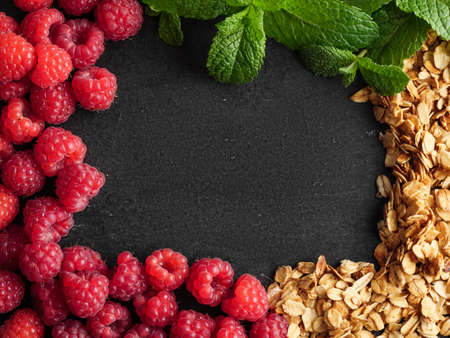 Granola, raspberries, peppermint leaves lie on a stone, copy space, top view.の写真素材