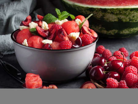 Fruit salad with watermelon, feta cheese, mint, raspberries and cherries on a gray background. Healthy eating.の写真素材