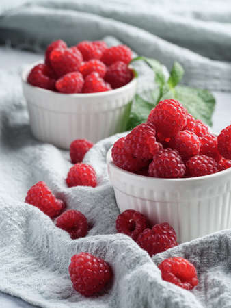 Fresh raspberries in small white cups on a table covered with cloth. Vertical photo, copy space.の写真素材