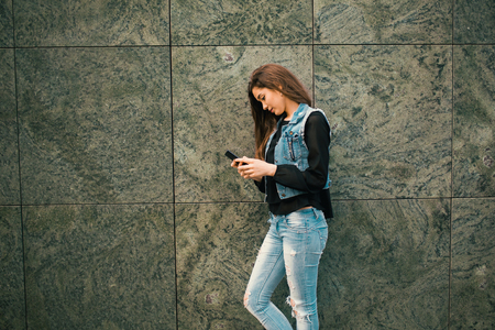 Beautiful teens talk to smartphone dressed in jeans, and have fun in the cityの写真素材