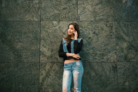Beautiful teens talk to smartphone dressed in jeans, and have fun in the cityの写真素材
