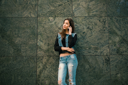 Beautiful teens talk to smartphone dressed in jeans, and have fun in the cityの写真素材