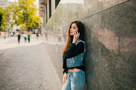 Beautiful teens talk to smartphone dressed in jeans, and have fun in the cityの写真素材