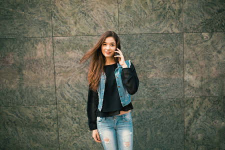 Beautiful teens talk to smartphone dressed in jeans, and have fun in the cityの写真素材