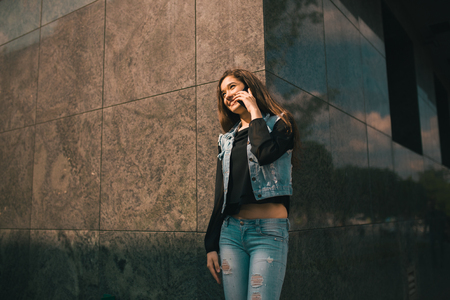Beautiful teens talk to smartphone dressed in jeans, and have fun in the cityの写真素材
