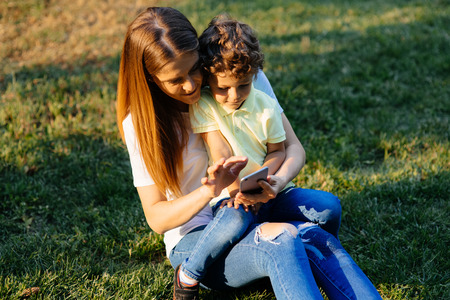 Mother and her baby, play cheerfully in the smartphone, outdoorsの写真素材