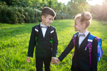 two beautiful school children hold their hand, with schoolbag, dressed in school uniform, outdoor, at sunsetの写真素材