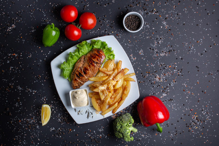 grilled baked chicken breast, fried potatoes with sauce, on black background with red tomatoes, red green peppers and broccoli, Lemon, top viewの写真素材