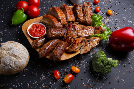 sausages and pork baked in the oven, on black background with tomatoes, red green peppers and broccoli, bread, top viewの写真素材