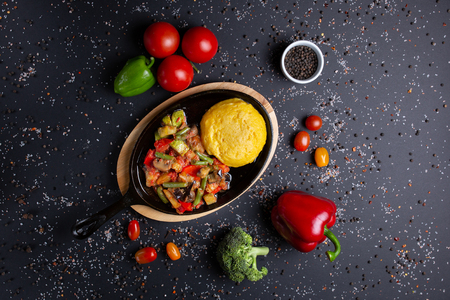 polenta with stew pan,  on black background, with tomatoes, red green peppers and broccoli, top viewの写真素材