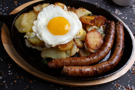 baked sausages with potatoes and fried eggs, on black background, top view, close upの写真素材