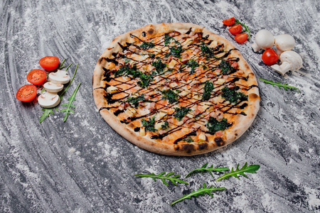 Delicious pizza with arugula, cheese tomato and bacon, decorated with sliced tomatoes and mushrooms, black background with flour, Top view. Banner, close-up, copy spaceの写真素材