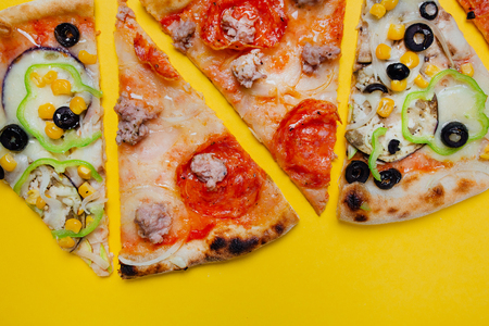 four slices of different pizzas, pepperoni,  sliced peppers, yellow background, Top view. Banner, close-up, copy-spaceの写真素材