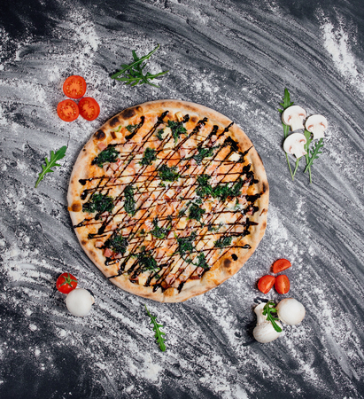 Hot meat pizza with salami, cream cheese Feta and Tomato Slices decorated with fresh greens, black background with flour, Top view. Banner, close-up, copy spaceの写真素材