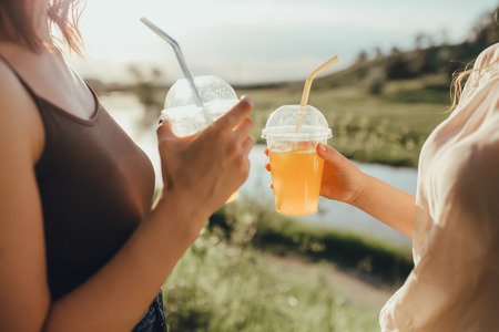 close up. girls with two plastic cups with orange juice, with straw, at sunset,  outdoorの写真素材
