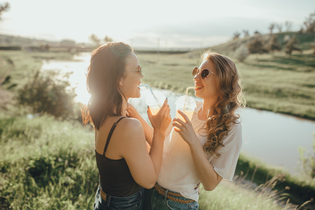 two beautiful girlfriends girls drink cocktail having fun summer, at sunset, positive facial expression, outdoorの写真素材