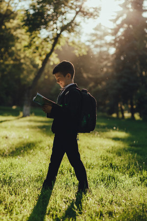 beautiful schoolboy portrait reads the book, is happy after school, profile view, outdoor, at sunset