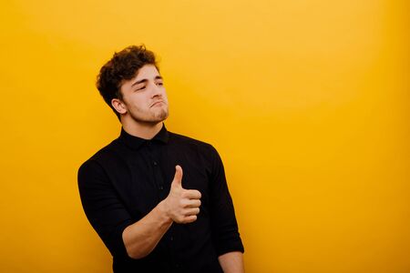 attractive and satisfied man, showing positive gesture with his thumb, satisfied human emotion, isolated on yellow backgroundの写真素材