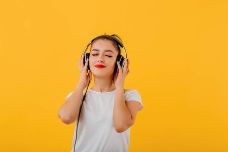 happy teenager listening to music on headphones with eyes closed, dressed in a white shirt,  positive facial emotion isolated on a yellow backgroundの写真素材